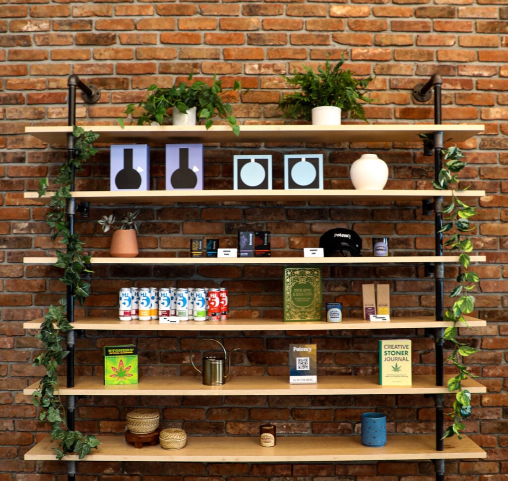 Product shelves in a cannabis dispensary against a brick wall with hats, drinks, and accessories.